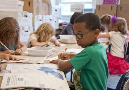 boy in green sweater writing on white paper
