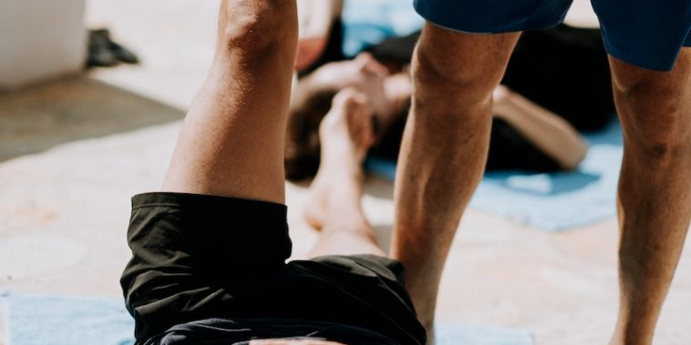 man lying on floor near man standing holding his leg