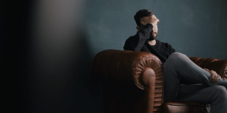 a man holds his head while sitting on a sofa