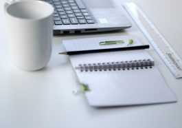 black pencil on ruled notepad beside white ceramic mug and gray laptop computer