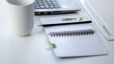 black pencil on ruled notepad beside white ceramic mug and gray laptop computer