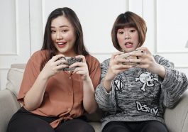 two women holding controllers sitting on sofa chair