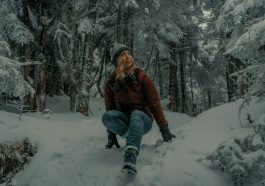 woman in brown jacket and blue denim jeans sitting on snow covered ground