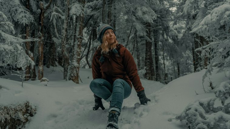 woman in brown jacket and blue denim jeans sitting on snow covered ground