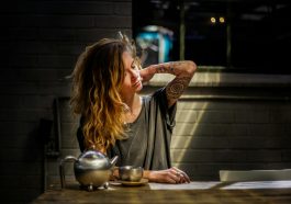 woman in gray top sitting beside gray tea pot and cup on brown wooden table