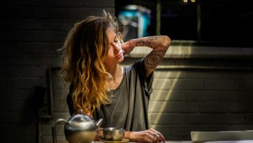 woman in gray top sitting beside gray tea pot and cup on brown wooden table