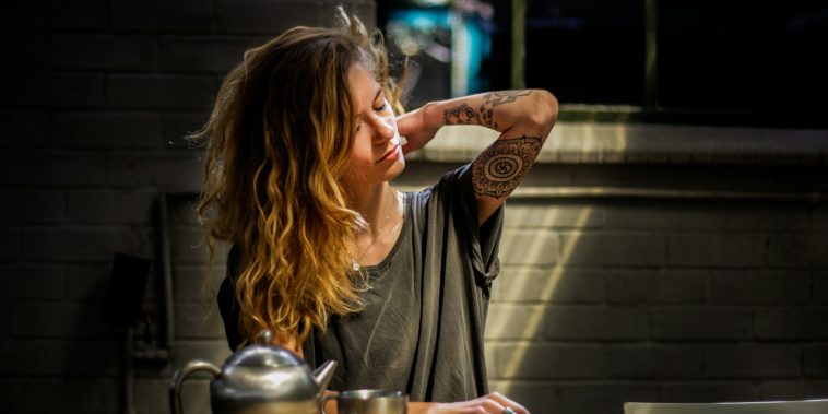 woman in gray top sitting beside gray tea pot and cup on brown wooden table